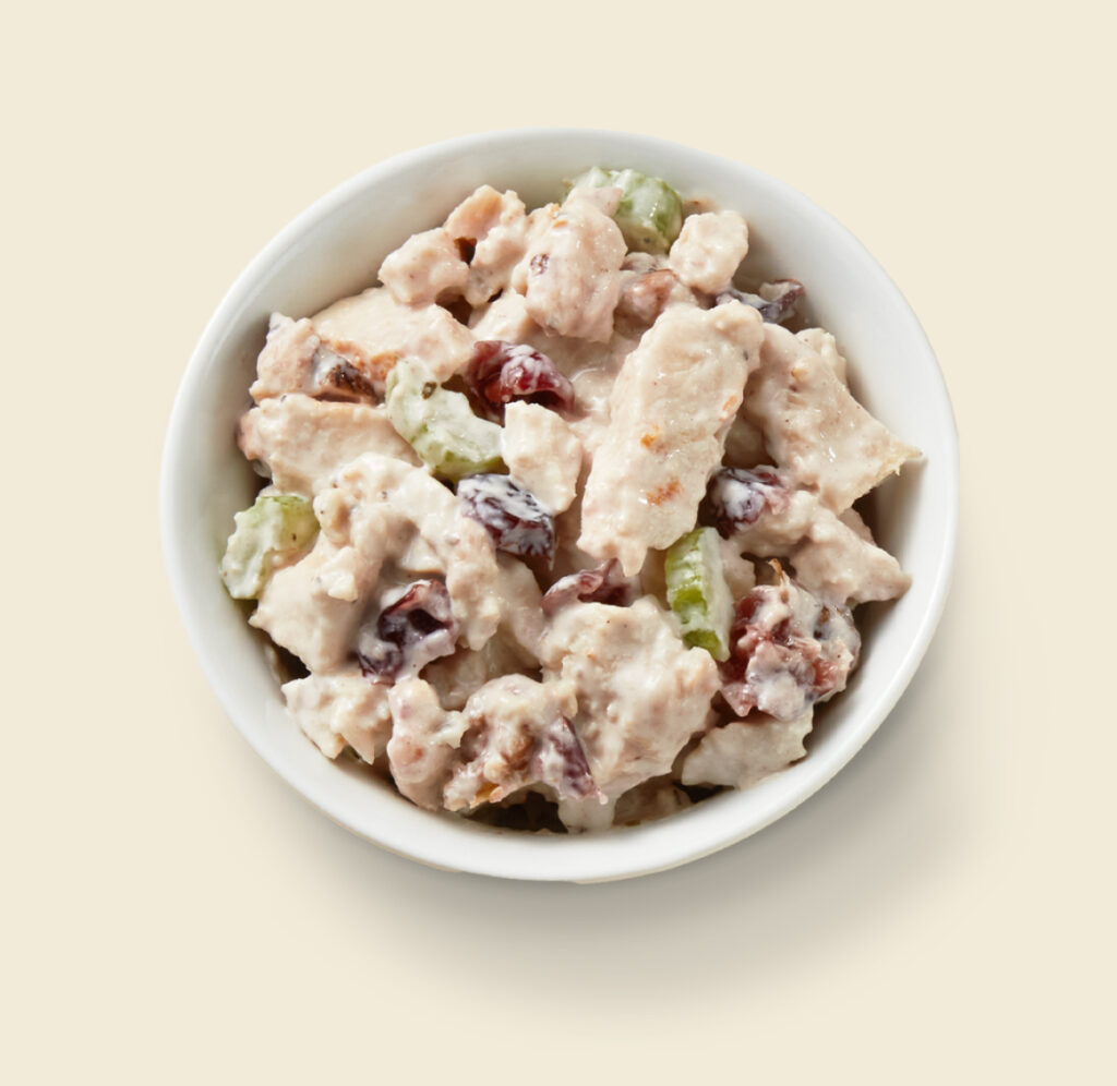 A bowl of creamy chicken salad with chunks of chicken, dried cranberries, celery, and walnuts in a white dish.